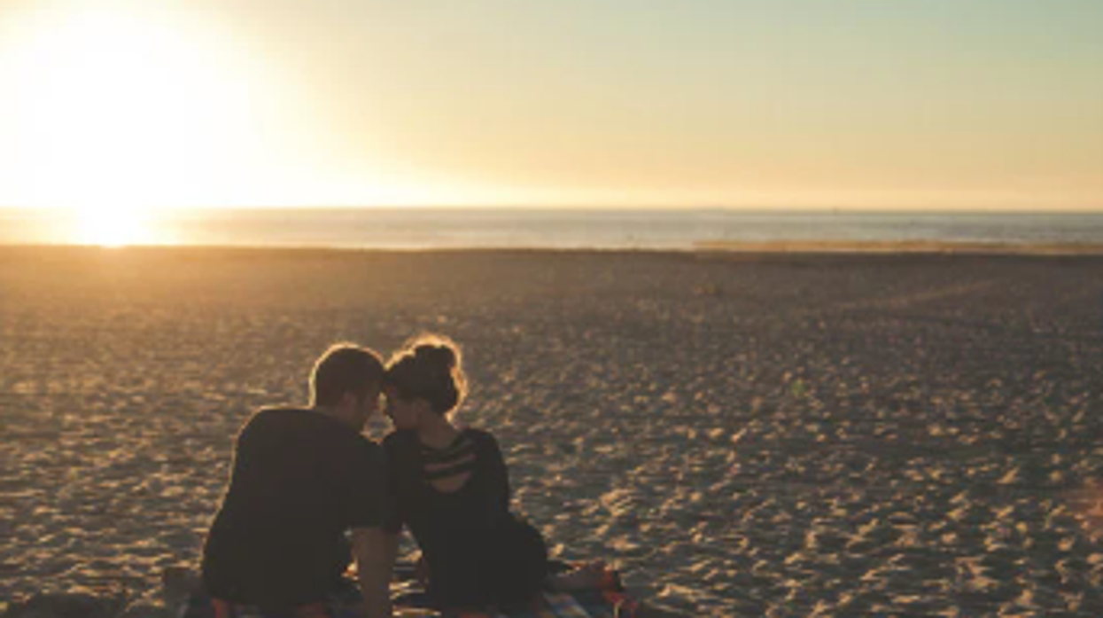 A couple sits on the beach with the ocean in the background