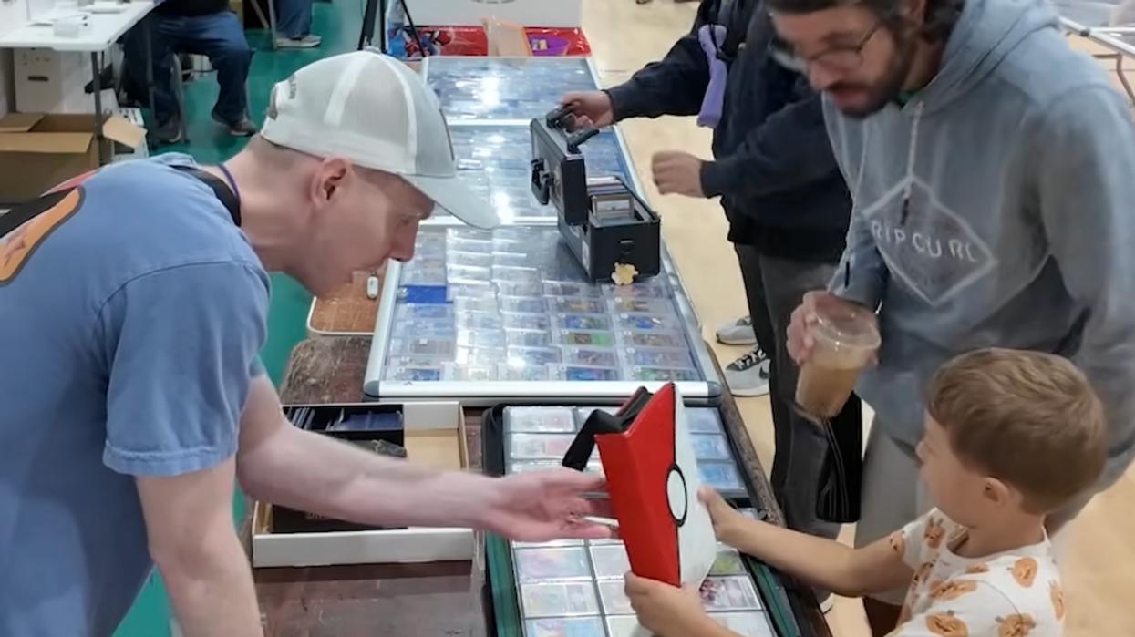 Coop's Collection giving a binder of cards to a little boy at a table while his dad watches.