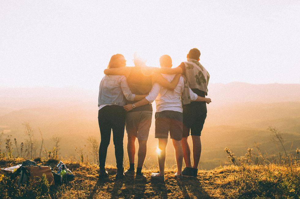 four people with their hands wrapped around each other shoulders look at the sunset in nature