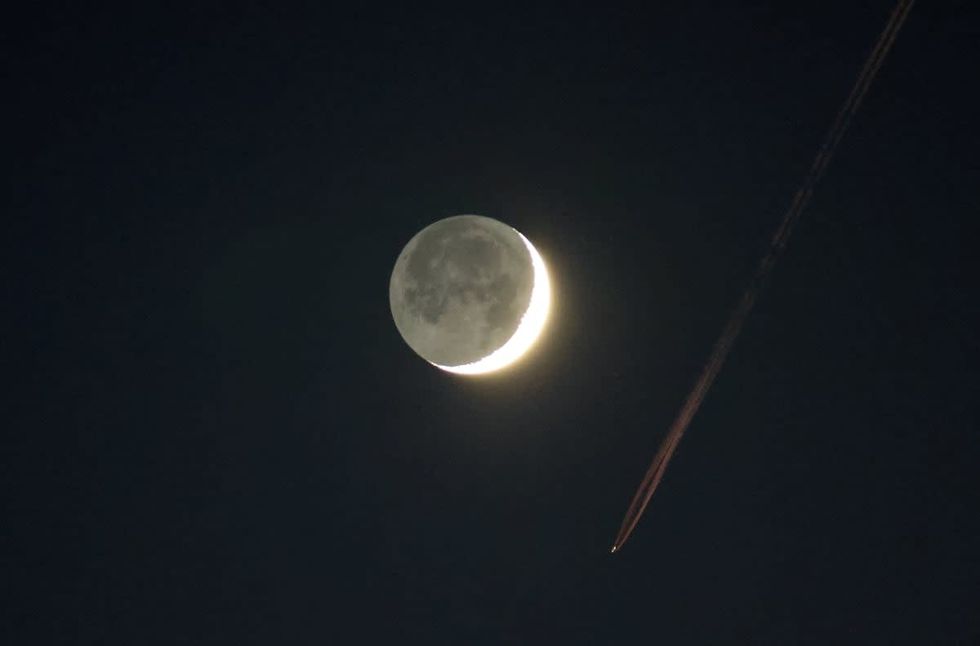 Image Source: An airplane contrail is lit by the setting sun as a waxing crescent moon illuminated with earthshine. (Photo by Gary Hershorn/Getty Images)