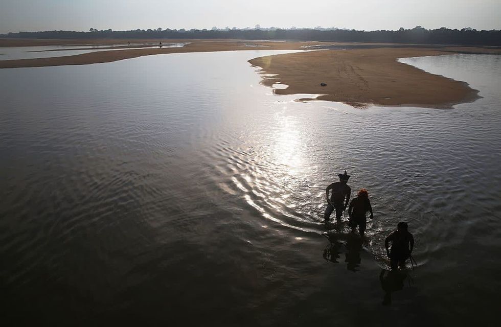 Members of the Munduruku indigenous tribe walk on the banks of the Tapajos River as they prepare a protest against plans to construct a hydroelectric dam on the river in the Amazon rainforest on November 26, 2014 near Sao Luiz do Tapajos, Para State, Brazil