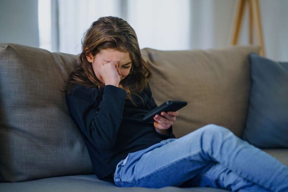 Representative Image Source: Small girl with smartphone sitting indoors on sofa, crying (Getty Images)