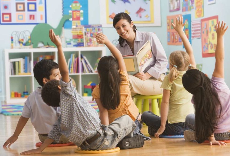 Representative Image Source: Teacher reading book in classroom, children (2-7) raising hands (Getty Images)