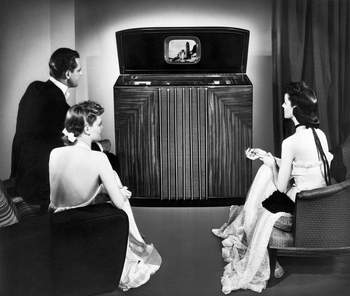 (Original Caption) Publicity handout showing formally dressed trio watching large console television. Undated photograph/illustration. (Photo by George Rinhart/Corbis via Getty Images)