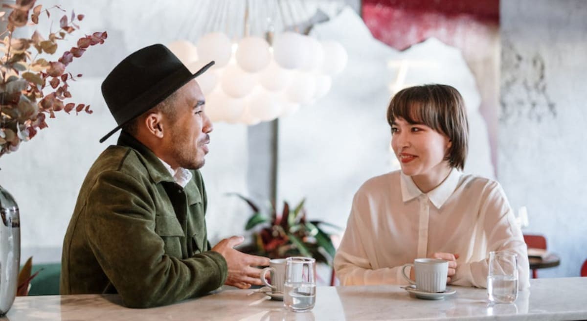 A man in a green jacket is talking to a woman in a white shirt. Via Cottonboro Studio/Pexels.