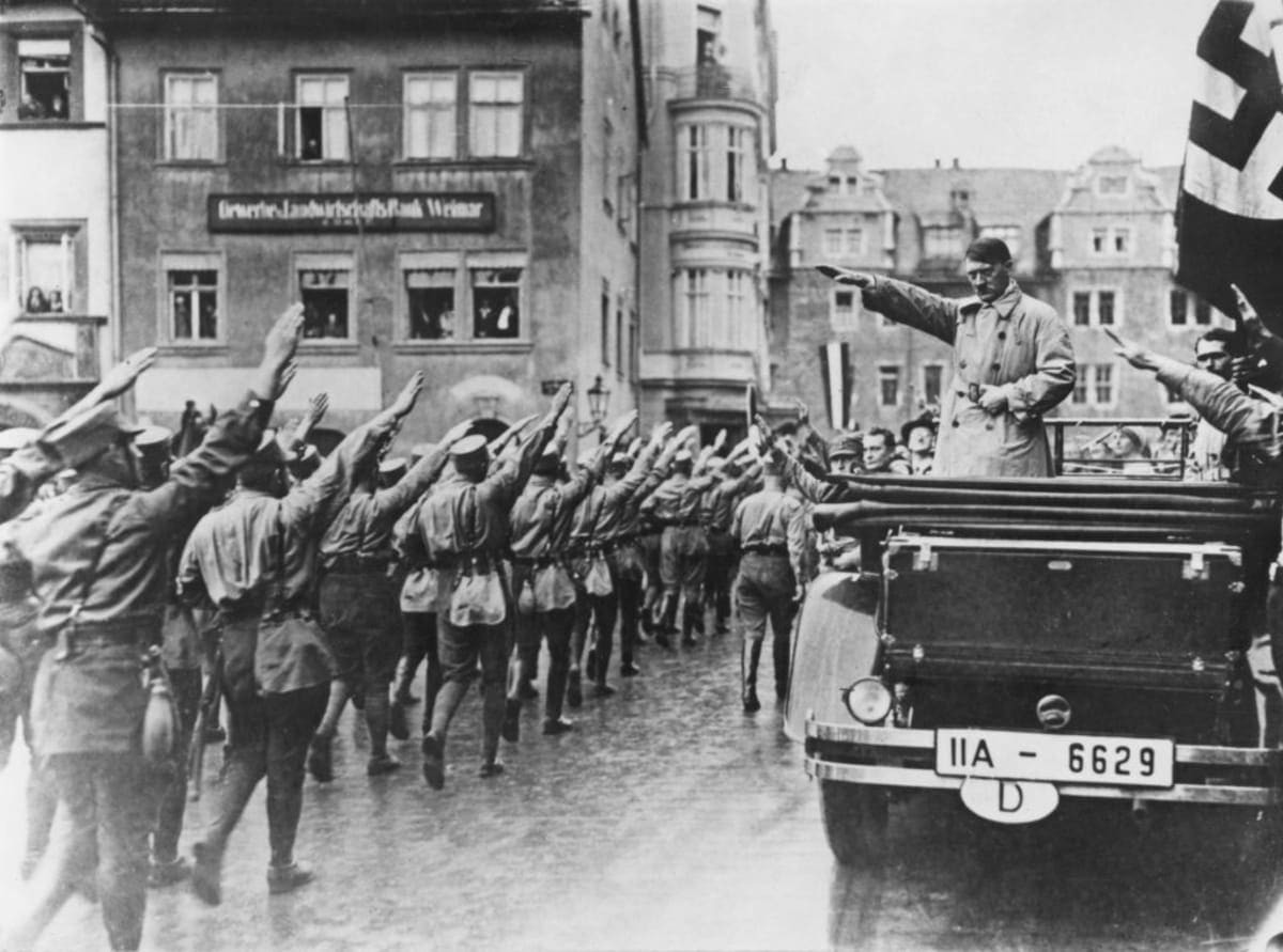 Image Source: Nazi leader Adolf Hitler takes the salute as Sturmabteilung (SA) paramilitaries march past in the market square in Weimar, Germany, 13th November 1930.  (Photo by Hulton Archive/Getty Images)