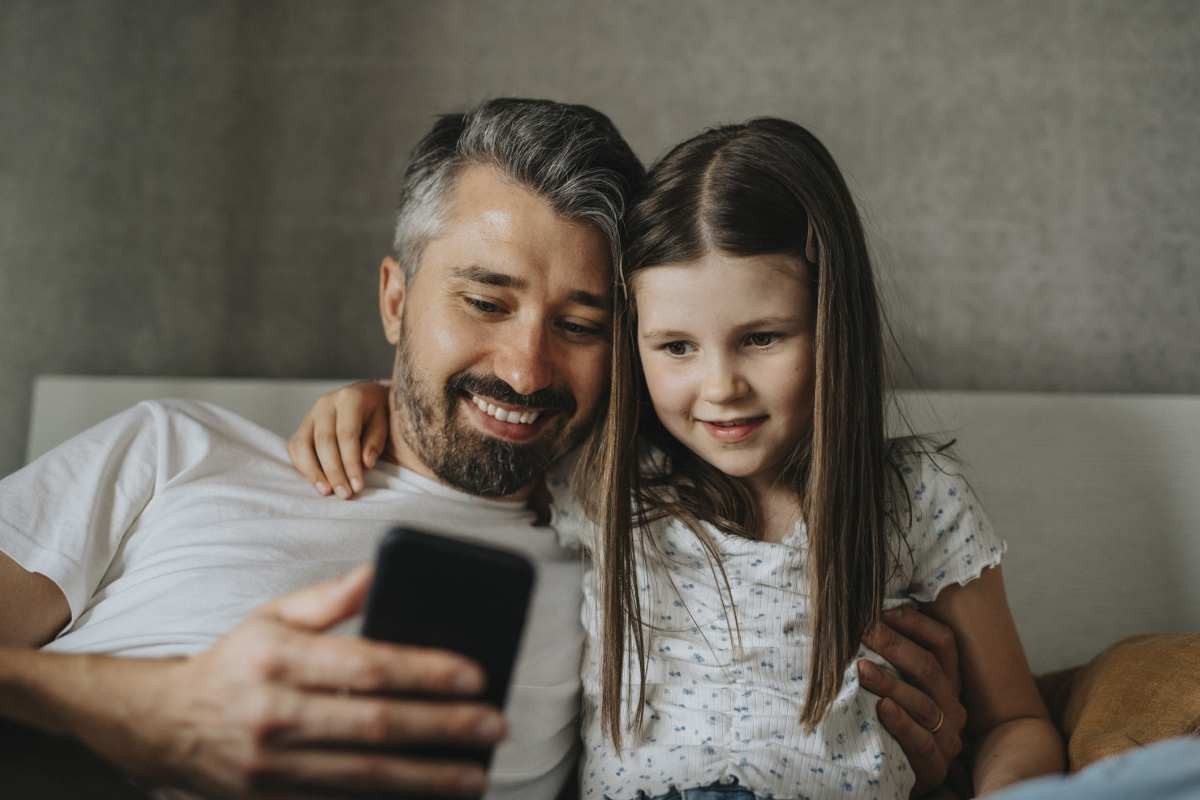 Representative Image Source: Smiling daughter with arm around father using smart phone at home (Getty Images)