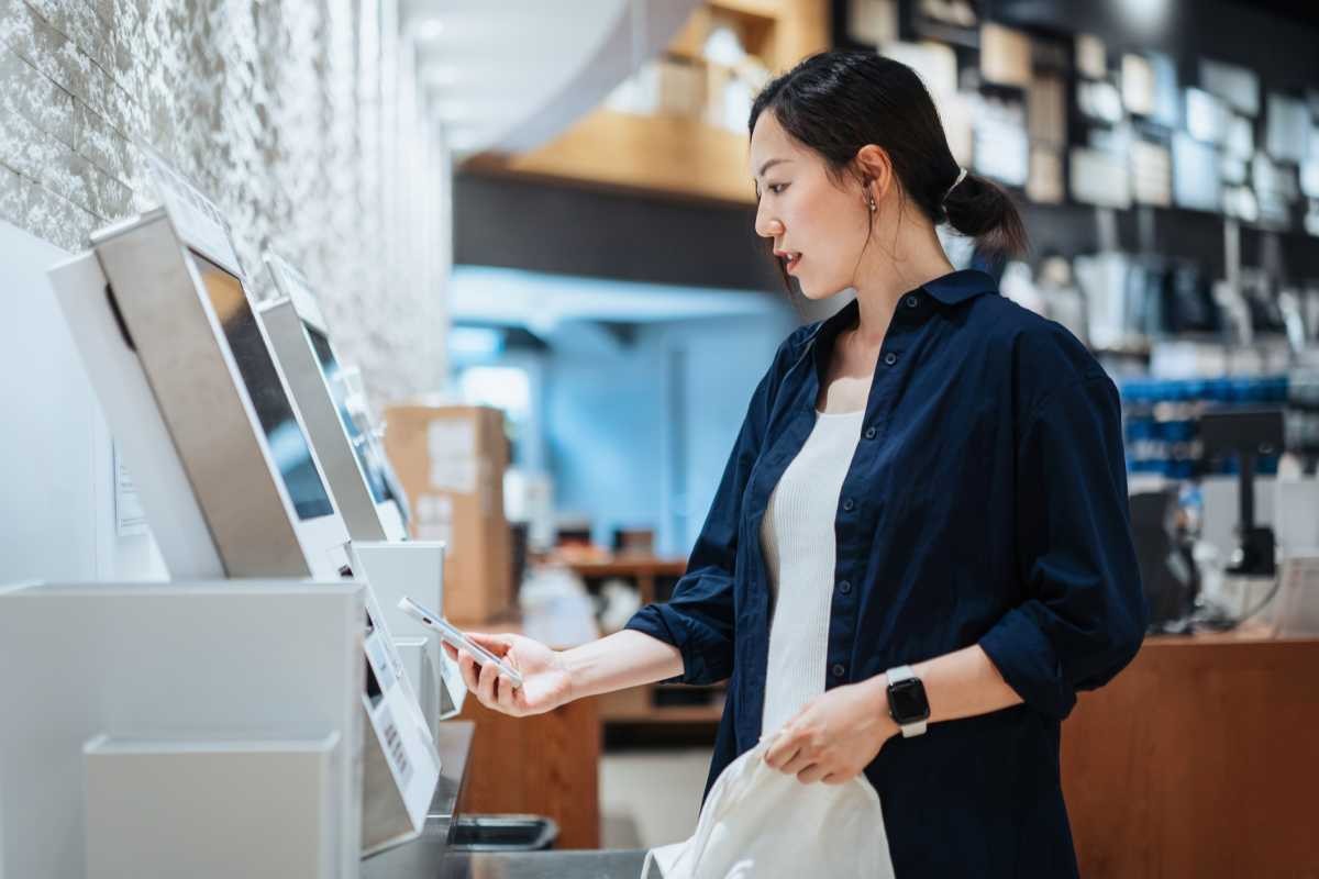 Representative Image Source: Young Asian woman with a reusable shopping bag, using contactless payment via smartphone to pay for her shopping at self-checkout kiosk in a store (Getty Images)