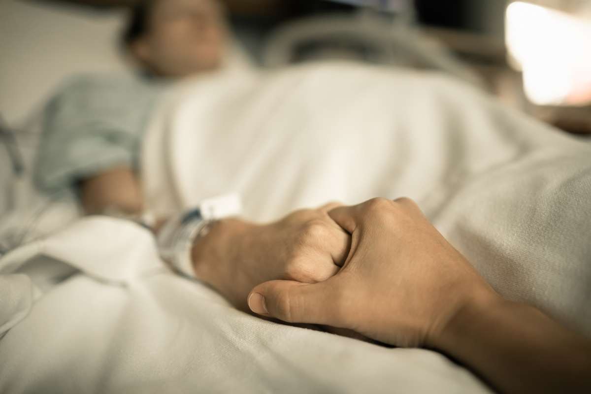 Representative Image Source: Man holding hand, giving support and comfort to woman, loved one sick in hospital bed. (Getty Images)
