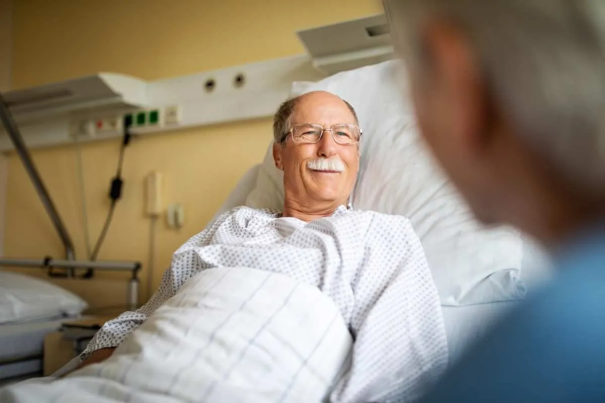 Senior man lying on hospital bed and talking with woman sitting by. Sick man talking with visiting wife in hospital room. (Representative Image Source: Getty Images | Luis Alvarez)