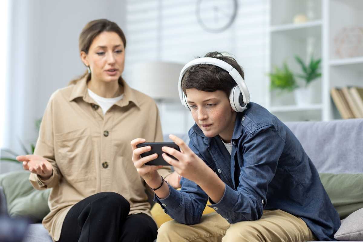 Teenage boy in headphones ignores woman and plays video games on phone (Representative Image Source: Getty Images | Photo by Liubomyr Vorona)