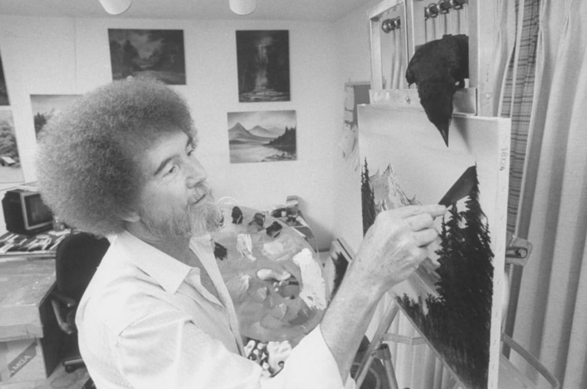 Image Source: TV painting instructor/artist Bob Ross painting one of his landscapes as his pet crow watches closely from its perch on top of easel in studio at home. (Photo by Acey Harper/Getty Images)