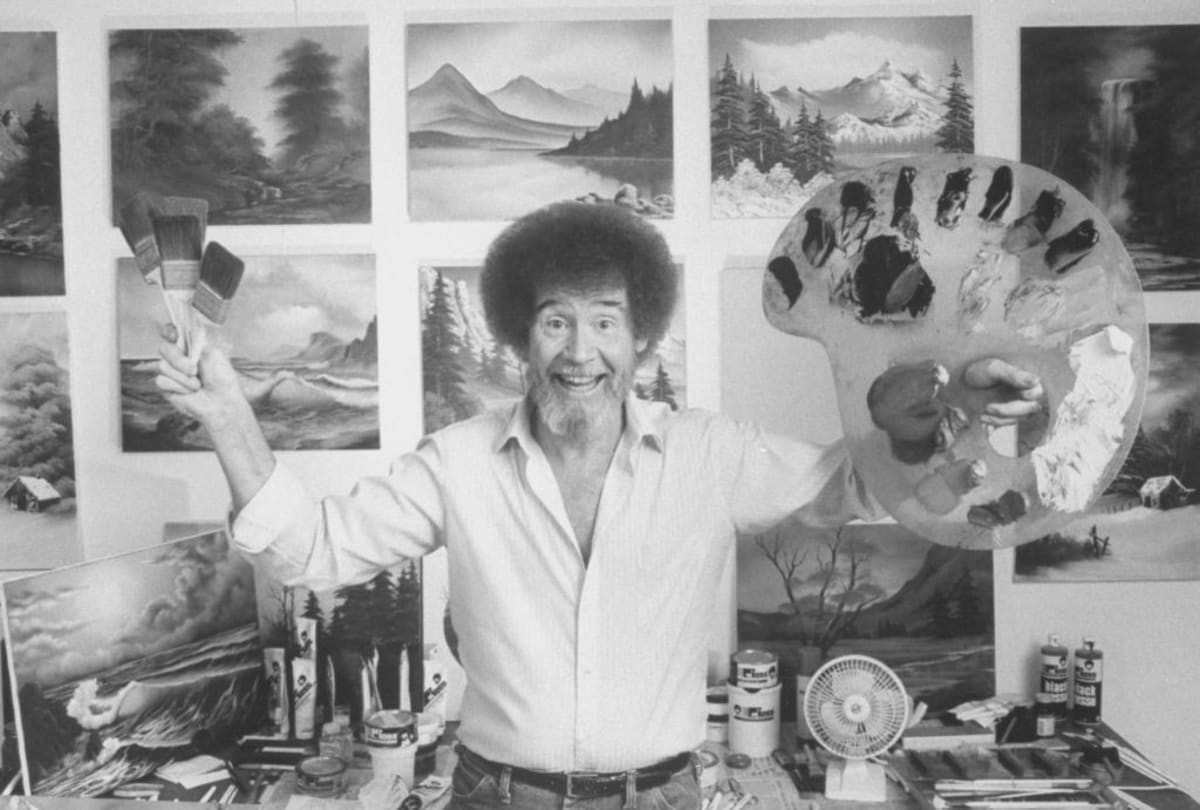 Image Source: TV painting instructor/artist Bob Ross jubiantly holding up paint pallette & brushes as he stands in front of wall covered w. his landscape paintings in his studio. (Photo by Acey Harper/Getty Images)