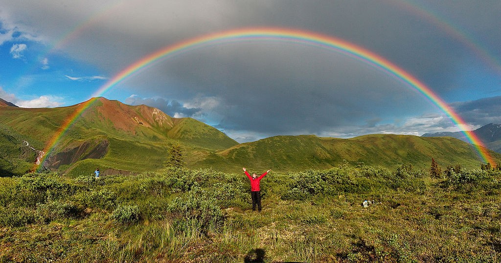 a double rainbow with a person in red standing in the middle raising their arms
