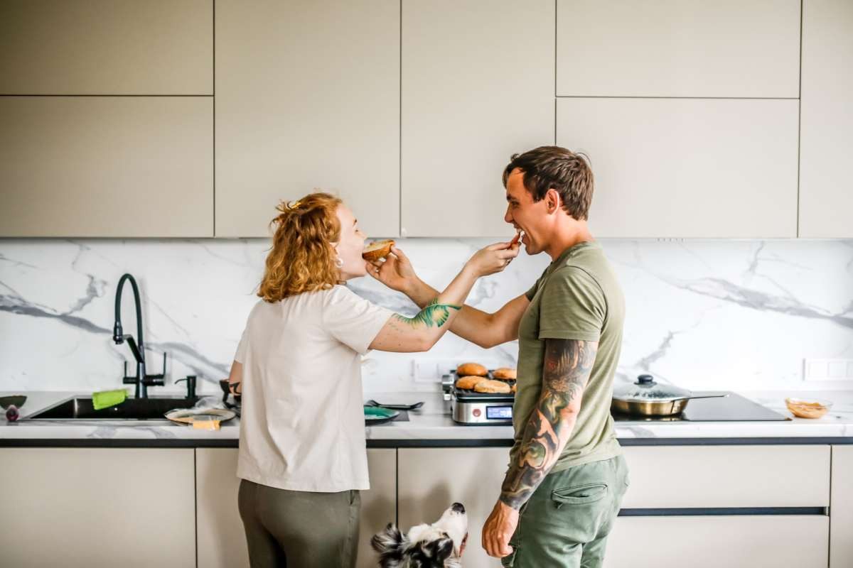 Adorable couple enjoys cooking together in their well-lit, modern kitchen, playfully sharing bites of food (Representative Image Source: Getty Images | Natalia Lebedinskaia)