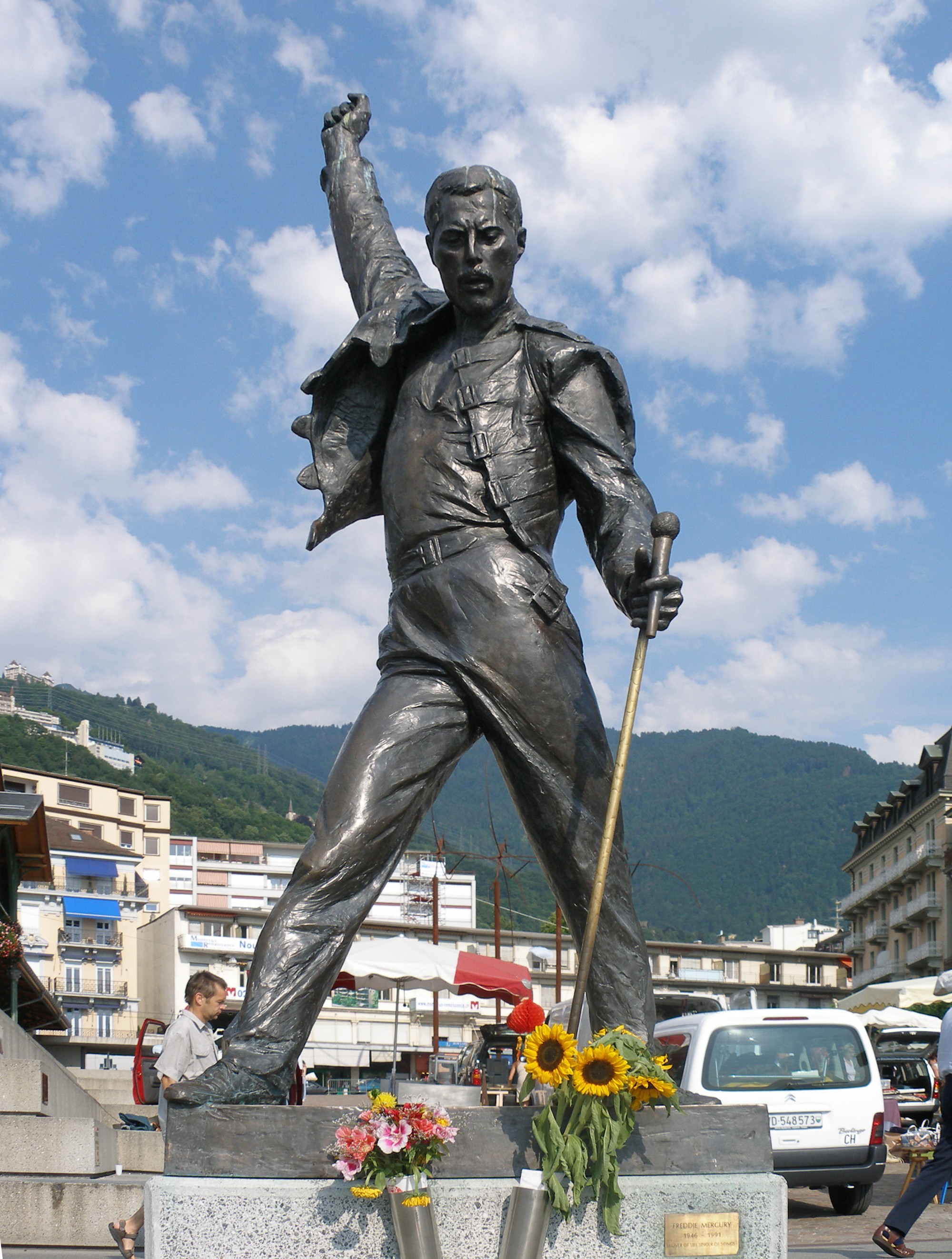 statue of Freddie Mercury in a bust street laden with flowers