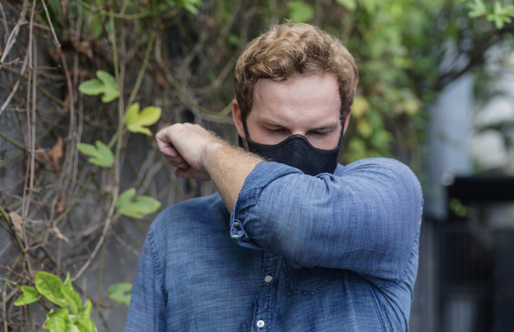 Man in a mask coughing into the crook of his elbow