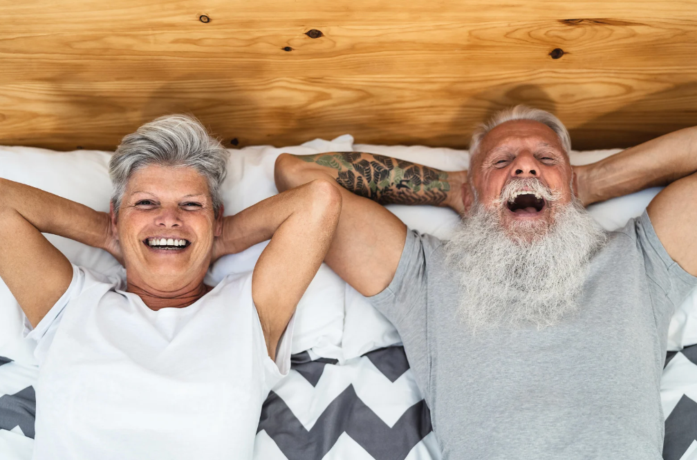 Old couple smiling in bed together, relaxing.