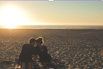 A couple sits on the beach with the ocean in the background