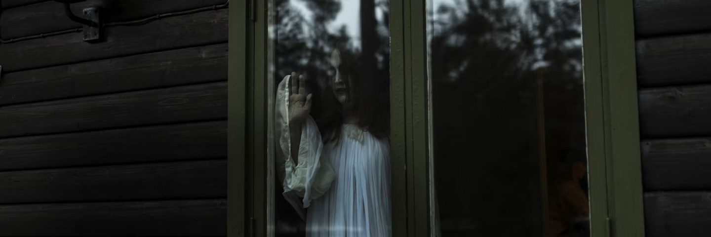 A ghostlike figure peers into a cabin through the glass windows.