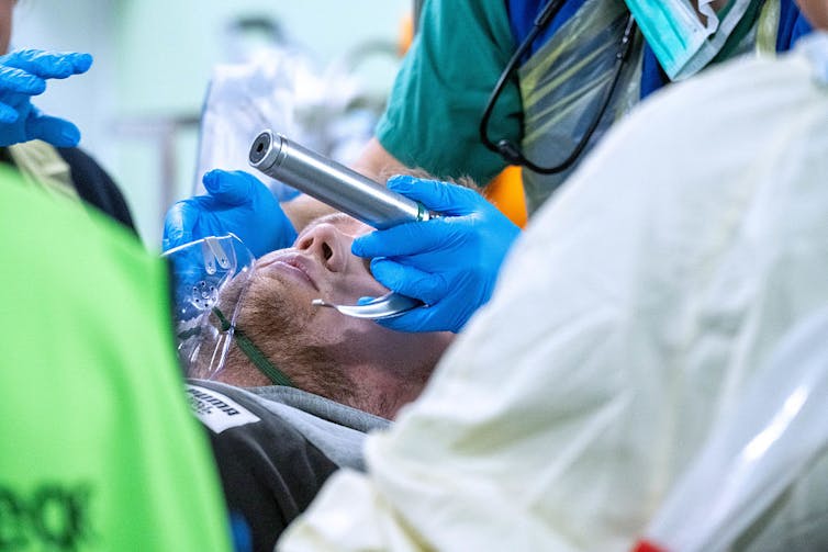 Doctor wearing blue gloves prepares to intubate a male patient.