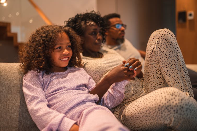 child, woman and man in pajamas seated on couch looking out of frame