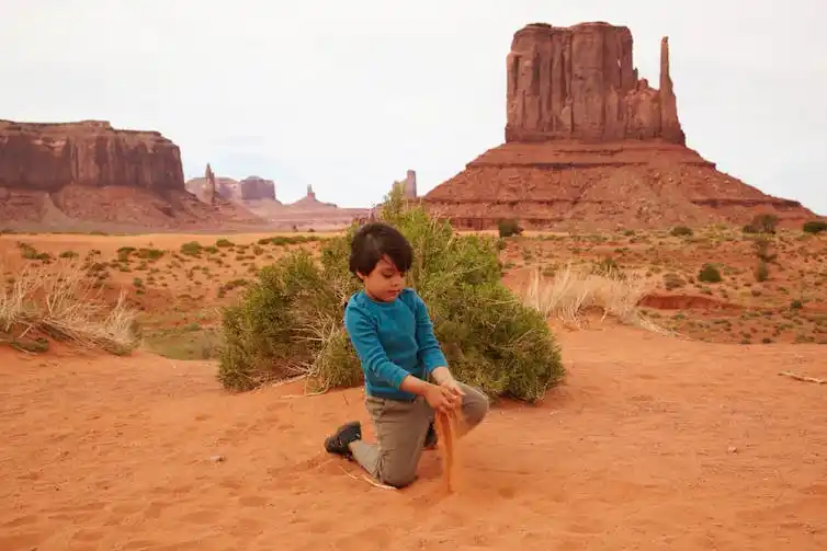 A child plays with sand in in front of a rock formation in Monument Valley