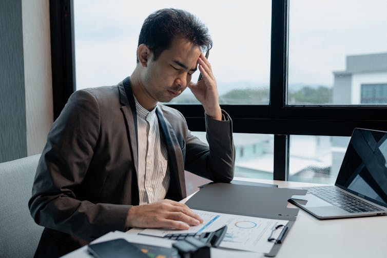 Young desk worker at a desk in an office, looking at charts, straining his eyes and holding up his head