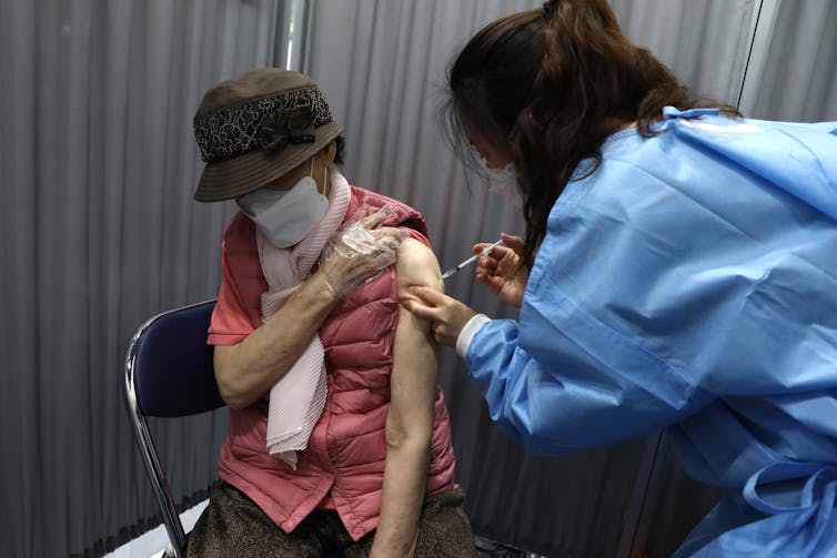 A nurse administers a vaccine shot to an elderly lady.