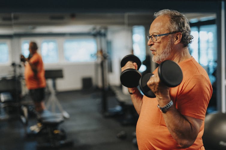 Side view of active senior man with dumbbells exercising at health club.