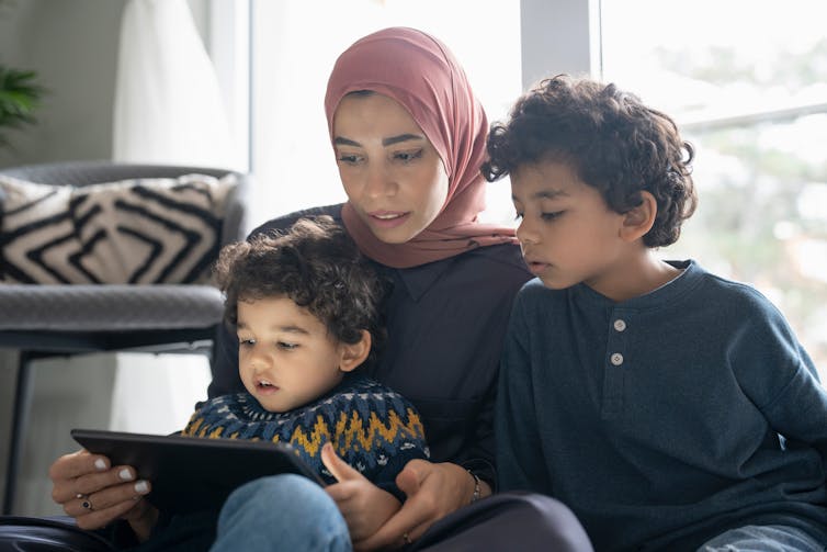 A woman and two small children look at tablet screen