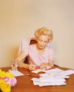 An older lady writes out checks to pay bills.